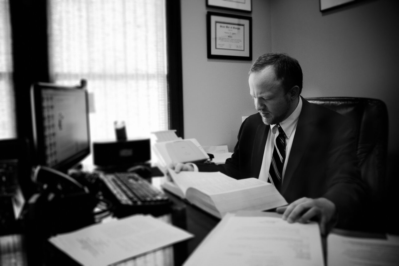 Graham W. Syfert at his desk reading a law book, with State Bar of Georgia certificate framed on the wall behind him
