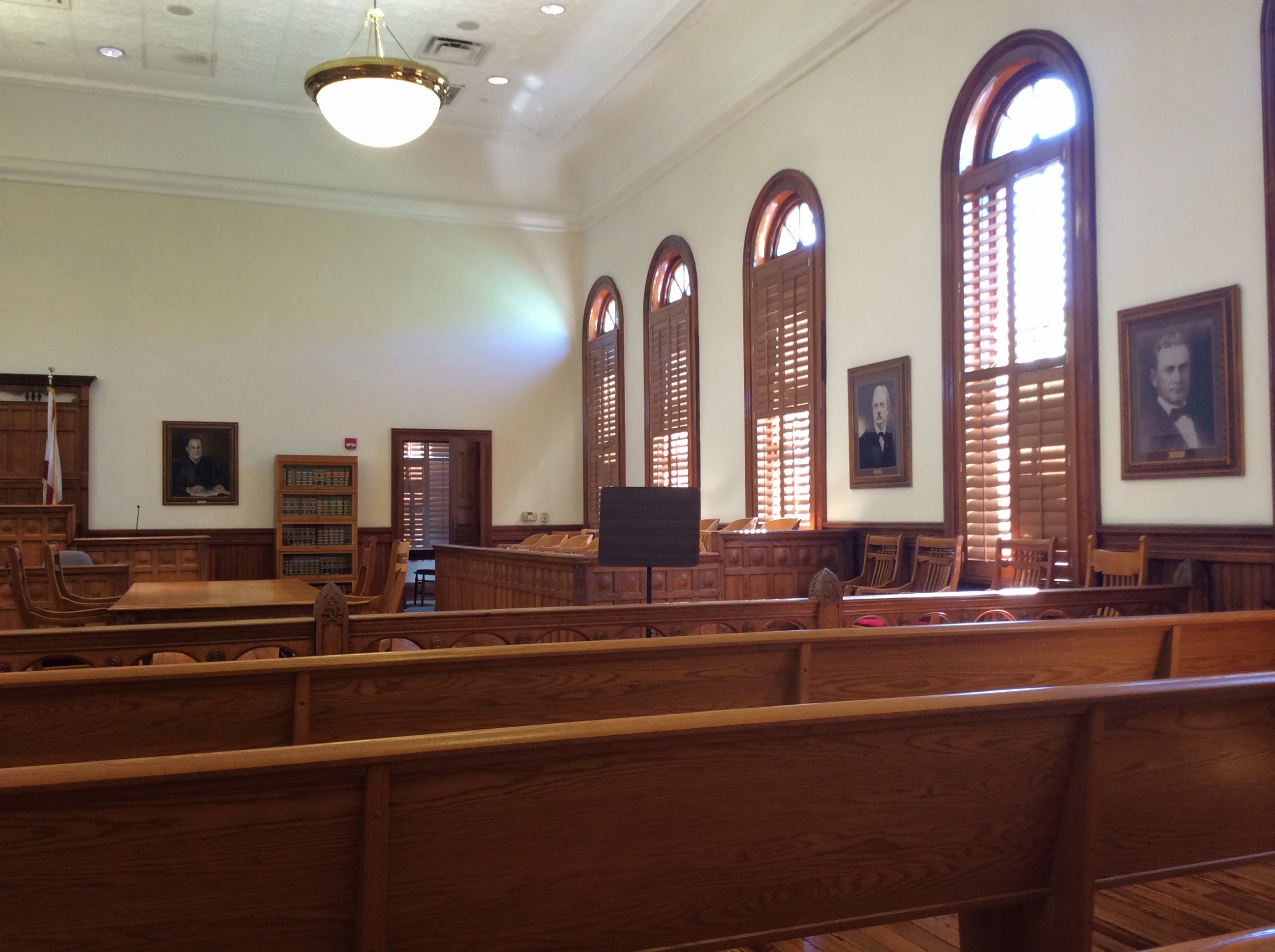 Interior of the Nassau County, Florida courtroom showing the gallery side, dark wood pews, and historical portraits hung between arched windows